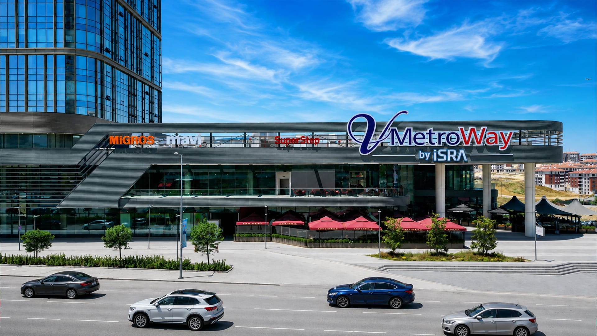 V Metroway'in gündüz görünümü: cephe boyunca uzanan V MetroWay by İSRA tabelası ve mağaza logoları, arkada ofis kulesi
